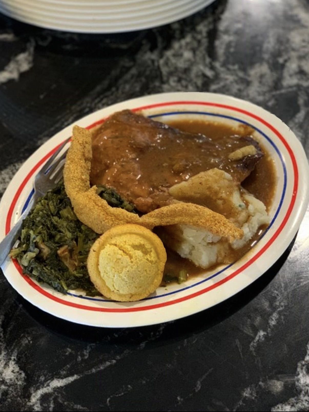 Smothered porkchop plate with fried fish, greens and cornbread